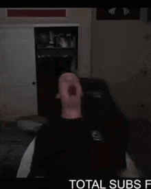 a man is sitting on a couch with his mouth open in a dark room with the words `` total subs '' below him .