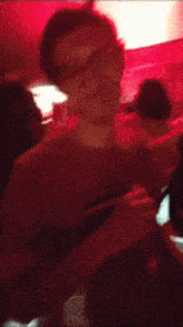 a woman wearing glasses and a red shirt is standing in front of a crowd of people .