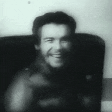 a black and white photo of a man sitting in a chair smiling .