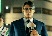 a man in a suit and tie is holding a microphone in front of him