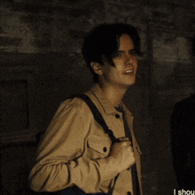 a man in a tan jacket is talking to another man in a dark room