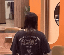 a woman wearing a black ac dc shirt is sitting at a table in a room .