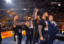 a group of men are standing in a wrestling ring and one of them is wearing a shirt that says one