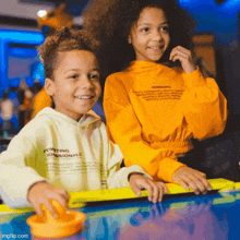 a boy and a girl are playing an arcade game and the boy is wearing a hoodie that says ingredients