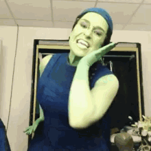 a woman with green paint on her face is wearing a blue top