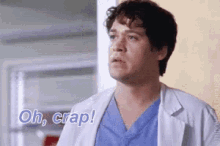 a man in a white coat and blue scrubs is standing in a room and says `` oh , crap ! ''
