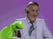 a man in a suit and tie is talking to a green kermit the frog puppet