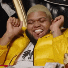 a man in a yellow jacket is sitting in a chair with his hands in the air and his tongue hanging out .