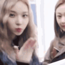 two girls are sitting next to each other and one of them is blowing a kiss at the camera .