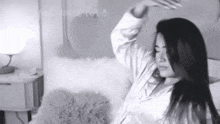 a black and white photo of a woman sitting on a bed with her arms outstretched .