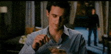 a man in a blue shirt is sitting at a table holding a glass of wine .
