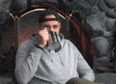 a man wearing a baseball cap is drinking from a metal mug