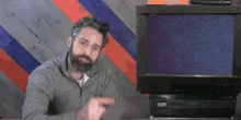 a man with a beard is pointing at something in front of a computer screen .