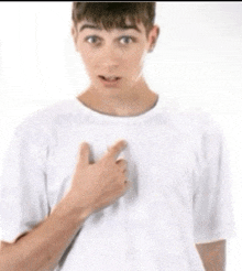 a young man in a white t-shirt is pointing to his chest