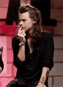 harry styles is sitting down with his hand on his chin .