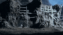 a man is standing in front of a large rock with a fence in front of it