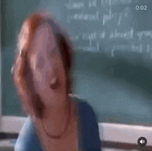 a woman with red hair is standing in front of a blackboard .