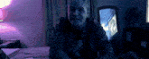 a man is sitting on a bed in a dark room with a purple light behind him .