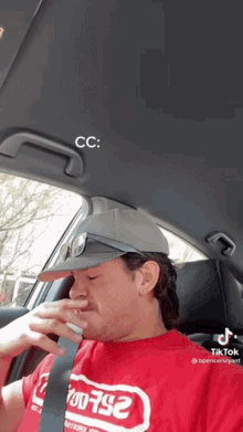 a man wearing a red shirt and a hat is sitting in a car .