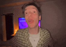 a man in a plaid shirt is making a funny face in front of a television