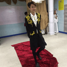 a man in a black jacket with gold embroidery is standing on a red carpet