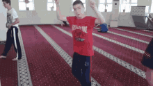 a boy in a red thrasher shirt is dancing in a room
