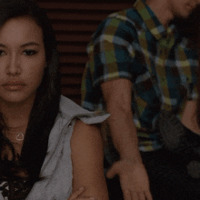 a woman wearing a necklace with a heart on it sits next to a man in a plaid shirt