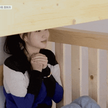 a woman in a blue and white sweater sits under a wooden fence
