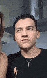 a young man wearing a black shirt and a necklace is standing next to a woman in a kitchen .