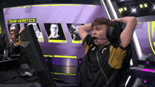 a man wearing headphones and a microphone is sitting in front of a screen that says " team heretics "