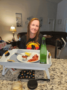 a woman wearing an official big foot shirt sits at a table with a tray of food on it