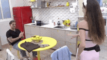 a man sits at a table in a kitchen talking to a woman in a pink dress