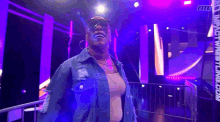 a woman wearing sunglasses and a denim jacket is standing in front of a purple wall with the word fite on it .