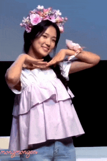 a woman wearing a flower crown makes a heart shape with her arms