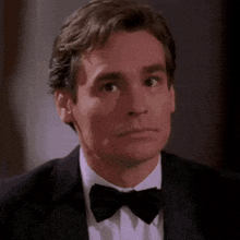 a man wearing a tuxedo and bow tie is looking at the camera .