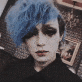 a man with blue hair and black makeup looks at the camera