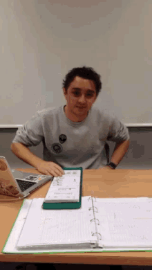 a man sitting at a desk with a binder and a laptop on it