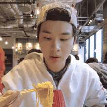 a man wearing a hat is eating noodles with chopsticks in a restaurant