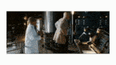 a man in a lab coat talks to another man in a dark room