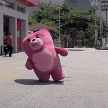 a pink teddy bear is walking down a street in front of a building