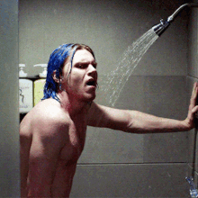 a shirtless man with blue hair is taking a shower in a bathroom