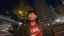 a man wearing a red coke shirt stands in front of a large building