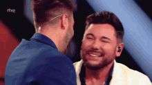 two men are smiling and laughing in front of a screen that says rtve