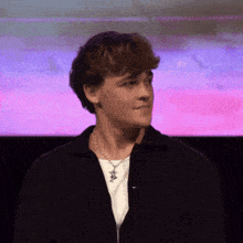 a young man wearing a black jacket and a white t-shirt is standing in front of a pink and purple background