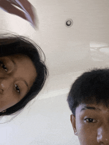 a man and a woman are looking at the camera with a ceiling fan behind them