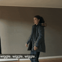 a woman in a parka is standing in front of a wall with the words wiggle wiggle wiggle below her
