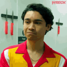 a man wearing a red and yellow shirt is standing in front of knives and a sign that says food preparation