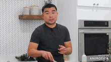 a man in a grey shirt is standing in front of an oven that says made in animonica