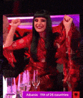 a woman in a red dress is sitting at a table with a sign that says albania 11th of 26 countries on it