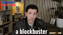 a man in a black jacket says a blockbuster in front of a bookcase